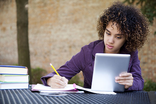 student reading from a tablet and writing in a notebook