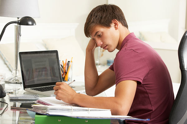 a student writing at his desk in front of a laptop