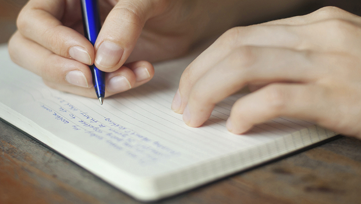 close-up of hands writing in notebook