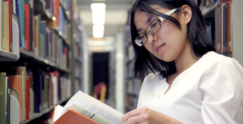 student reading from a book in a library
